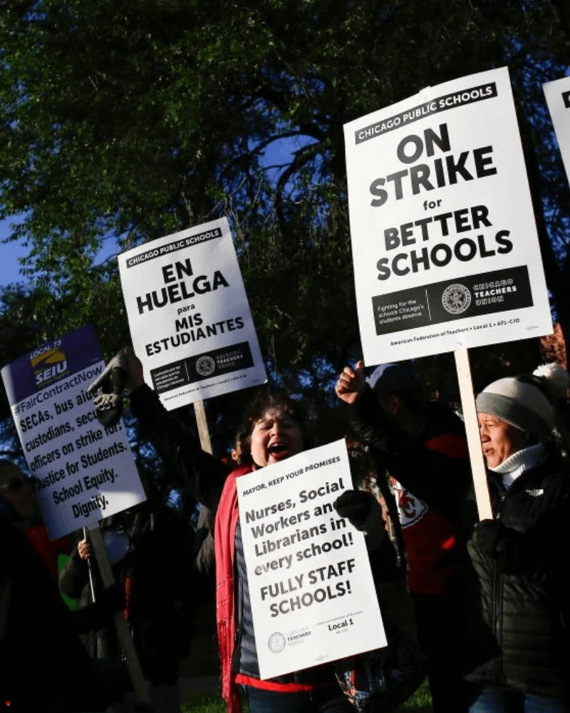 A group of people holding protest signs, including messages in English and Spanish, outside a building, advocating for better schools and staffing.